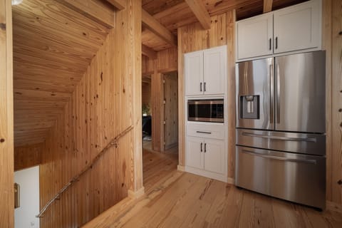 A kitchen area with wood paneling, featuring a built-in microwave, cabinetry, and a stainless steel refrigerator next to a staircase.