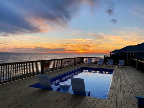Stunning oceanfront pool deck captures dramatic sunset views over the water, with comfortable lounge seating surrounding the pristine swimming area.