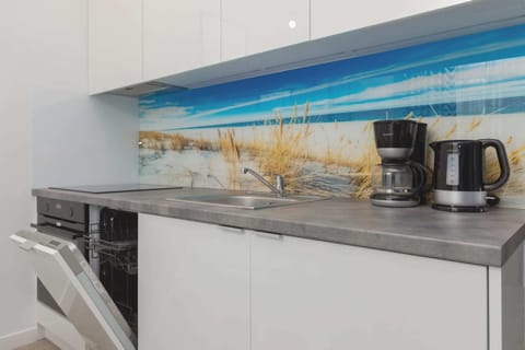 A fully equipped kitchen with a backsplash featuring a seashore mural. The space includes a kettle, microwave, and storage cabinets.