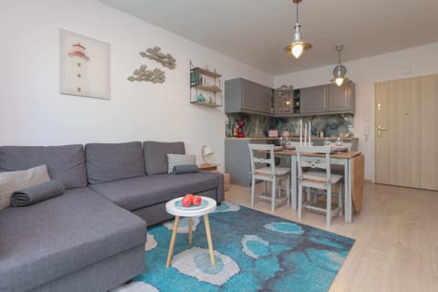 A modern living room featuring a gray sofa, a glass coffee table, and colorful artwork. The space is filled with natural light coming from large windows.