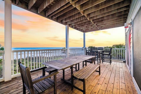 A covered oceanfront deck offers outdoor dining beneath striking architectural beams, with a tranquil beachfront and sunset views as your backdrop.