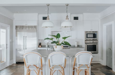 Kitchen island with three bar stools, thermador refrigerator, stove and oven on the far wall.