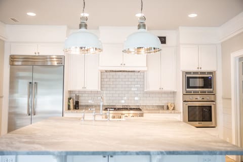 Modern kitchen with stainless steel appliances, white cabinets, tile backsplash, a large island, and two overhead lights.