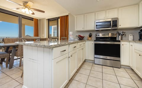 Bright kitchen area featuring granite countertops, modern appliances, and a dining space with woven chairs and a view