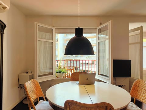 The dining area features a round table with four chairs, offering a comfortable space for enjoying meals. A large window with sheer curtains allows for ample natural light. A unique black lampshade hangs above the table, adding a touch of modern design.