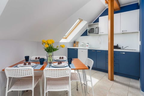 A bright dining area with a white table and chairs, situated next to a fully equipped kitchen with blue and white cabinets.

