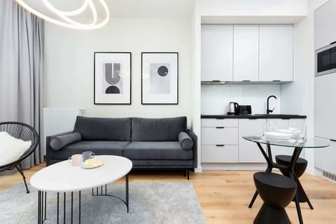 A spacious living room featuring a modern gray sofa, a white coffee table, and minimalist framed pictures on the wall. Bright colors and a large window add a sense of openness.