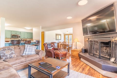 Spacious living area with large mounted flat screen TV, hardwood flooring, access to the private balcony, wood burning fireplace and ample seating.