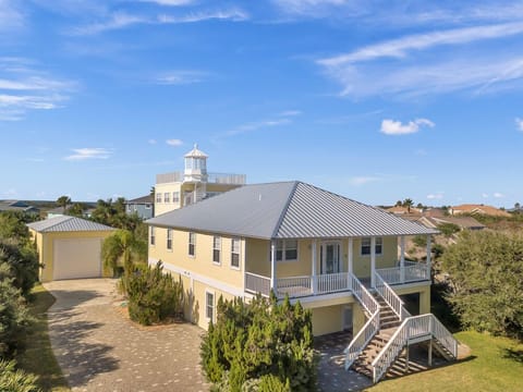 Charming coastal home with raised porch, palm trees, and bright exterior.
