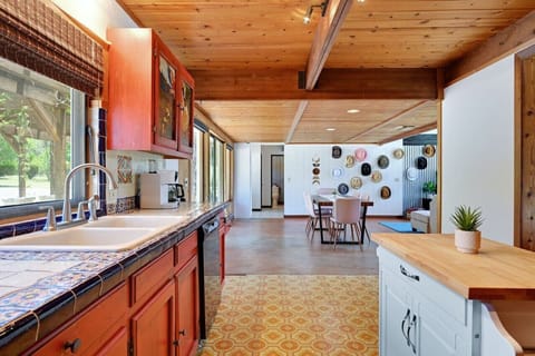 Colorful, tile‑topped kitchen at Road Runner Lodge opens to the dining area and hat wall—cook together while enjoying Hill Country views.