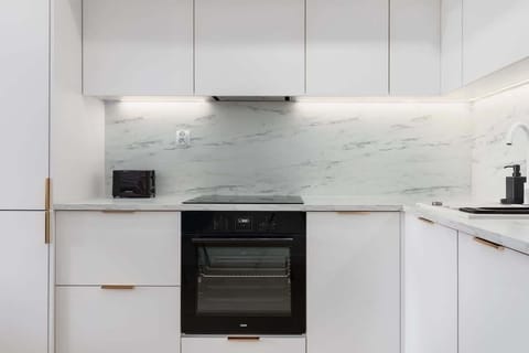 A sleek white kitchen with minimalist cabinetry, a black oven, and a marble backsplash, offering a sophisticated cooking area.