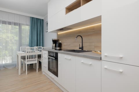 A small kitchenette with white cabinets, a wooden backsplash, and a dining table nearby. The blue curtains add a pop of color.