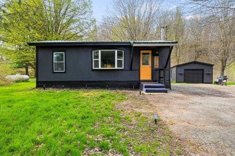 Welcome to your peaceful retreat: a modern cabin nestled among the lush greenery of the Finger Lakes, complete with a charming orange door that promises a cozy, inviting stay. The cabin features expansive windows that flood the interior with natural 