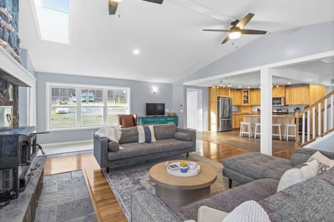 Expansive open living room space featuring plush couches, a warm fireplace, ample natural lighting, and inviting, cozy furnishings for a welcoming atmosphere.
