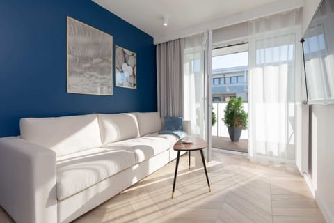 Modern living room space with a white sofa and a light floor with a contrasting blue wall.