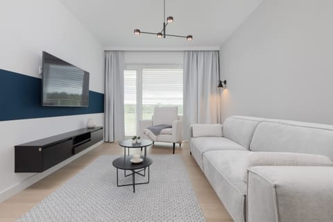 A spacious living room with a comfortable sofa, a coffee table, and a large TV mounted on the wall.
