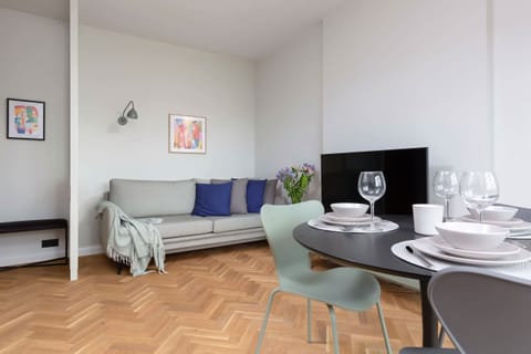 A cozy living room with a stylish sofa, round dining table, and a vibrant wooden floor.
