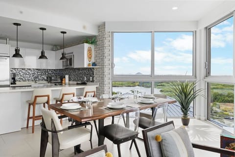 This open-concept living and dining space welcomes you with floor-to-ceiling windows framing serene views. Gather around the elegant dining table or unwind on the plush sofa as natural light fills your retreat.