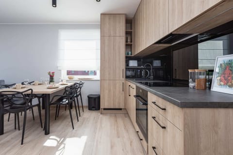 A modern kitchen with wooden cabinetry, a sleek black countertop, and a dining table.
