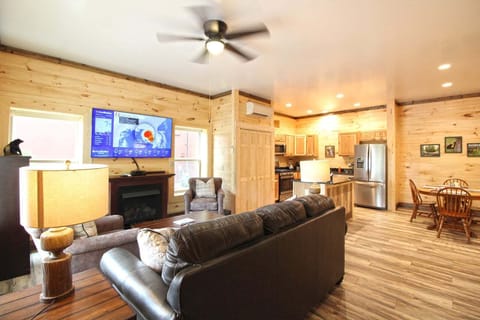Wide view of the open-concept living room and kitchen featuring leather seating, wood interior finishes, and stainless appliances. Pet-friendly cabin accommodations in Bryson City near Great Smoky Mountains National Park.