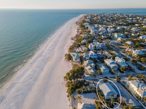 Stunning aerial view captures pristine white sand beach meeting turquoise waters, with charming coastal homes nestled among palm trees.