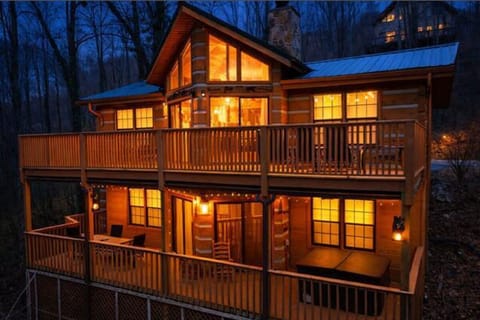Rustic mountain cabin glows warmly at dusk, nestled among towering trees with wraparound decks perfect for mountain evenings.