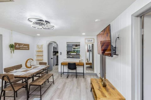 The living room is a modern and cozy space that combines a dining area and a relaxing zone. It features a wooden table with chairs and a bench, a desk for working or studying, a sofa bed, a TV, and stands out for its excellent lighting