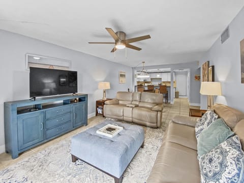 Open living room with TV, blue media console, beige sofas, and ceiling fan