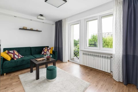 A living room with a green sofa, round coffee table, and large glass doors leading to a balcony.