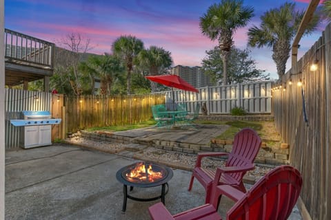 Enjoy the backyard at sunset, complete with comfortable seating under an umbrella and soft Edison lights overhead, offering a serene and inviting atmosphere for unwinding.