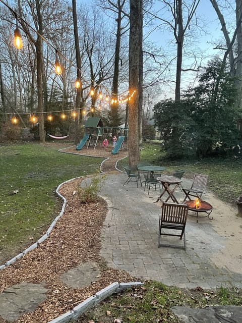 Large back yard with patio and string lights, swing set and trampoline.