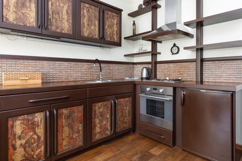 A rustic kitchen featuring dark wooden cabinets with intricate patterns, a brick-style backsplash, and modern appliances, combining a vintage aesthetic with functionality.