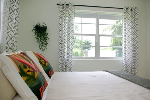 King size bed in airy bedroom with view of front yard with coconut tree.