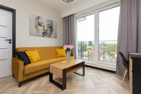 A stylish living room featuring a mustard-yellow sofa, a wooden coffee table, and large windows with plenty of natural light.
