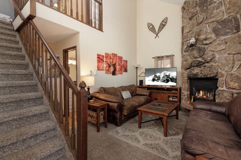 Cozy up in your spacious living room with warm leather seating, crackling stone fireplace, and rustic mountain charm perfect for relaxing evenings.