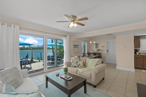 Indoor meets outdoor—bright living area with sliding doors opening to the bay, cozy sofa, smart TV, and calming coastal décor.