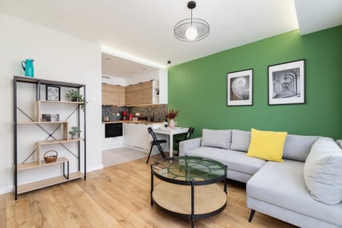 A stylish living room with a green accent wall, a cozy gray sofa, and a round glass coffee table, complemented by modern decor.

