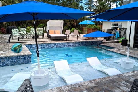 Pool with in-water lounges, umbrellas and owners home in background