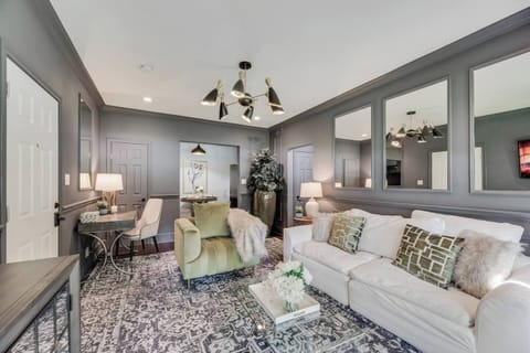 Open Living Room . In the corner, you'll find a dedicated office workspace, perfect for getting some work done. Mirrors on the walls enhance the natural light, while a beautiful chandelier adds a touch of elegance and warmth to the room.