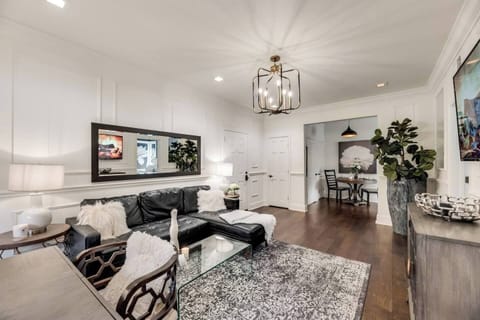 The living room offers a bright and inviting space, with a cozy black sectional couch. In the corner, you'll find a dedicated office workspace, perfect for getting some work done. A beautiful chandelier adds a touch of elegance and warmth to the room.