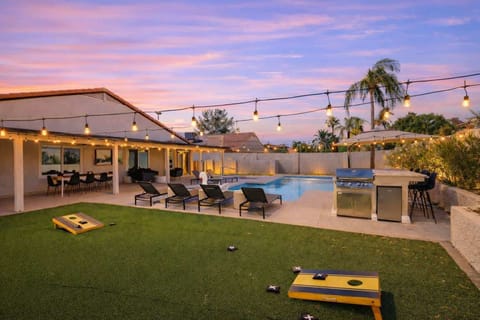 Backyard with putting green, corn hole, BBQ, bar seating, pool, jacuzzi, loungers, outdoor dining table and TV.