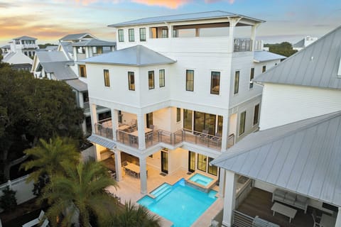 Stunning multi-level coastal home featuring a sparkling pool and spacious covered porches, nestled among palm trees in an upscale neighborhood.