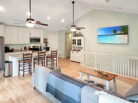 75" TV in living room with open kitchen, large sectional couch and deck access