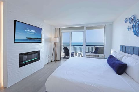 Wake up to breathtaking ocean views from your cozy bedroom retreat, featuring a plush bed, flat-screen TV, and private balcony access for the perfect blend of comfort and coastal charm.