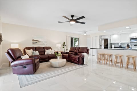 Relax in the inviting living room featuring a soft sofa and easy flow to a green-filled patio and sparkling pool.