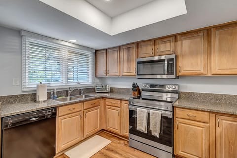 - Stainless appliances and granite countertops highlight this U shaped kitchen
- Natural wood cabinetry and overhead lighting create a bright, functional space
- Large window over sink offers a peaceful view while prepping meals