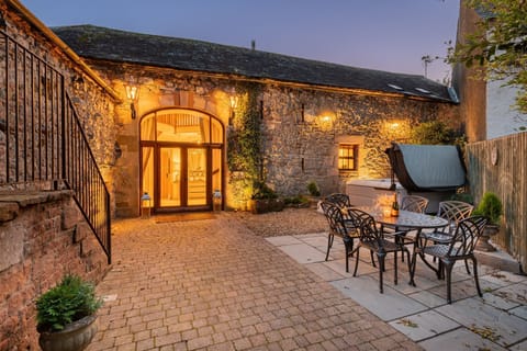 The private patio at night with a hot tub and a dining table and chairs at Rose Walls, Lake District