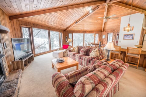 Cozy living room with large windows, stone fireplace, and comfy seating.