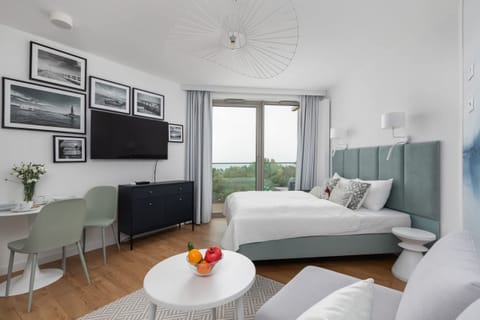 A bright, modern studio with a comfortable bed, a round coffee table, and large windows overlooking the outdoors.