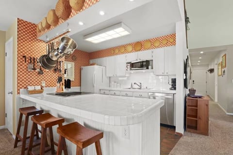 The kitchen is a bright space with a sleek, white tile backsplash and cabinets, large countertops for meal prep, and great views over the living and dining area.
